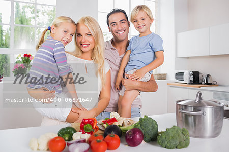Children in their parents arms in the kitchen preparing vegetables