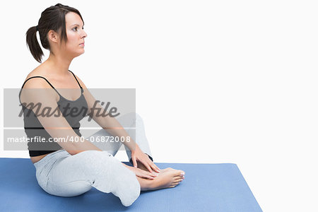 Side view of young woman sitting in yoga position on exercise mat over white background