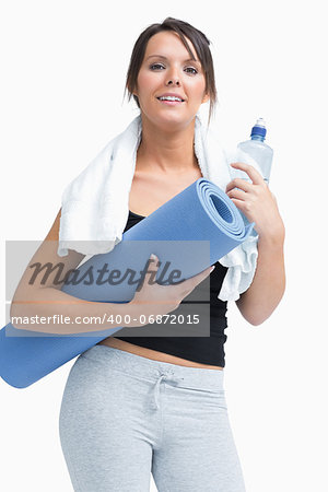 Portrait of young woman in sportswear holding water bottle and mat over white background
