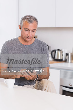 Mature man touching his smartphone in the kitchen