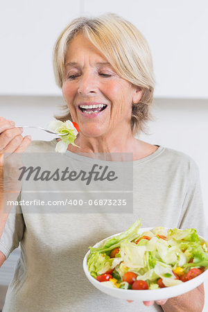 Mature woman eating salad in the kitchen
