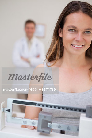 Smiling woman on the scale being supervised by doctor