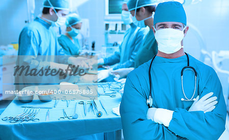 Surgeon standing with arms crossed with surgery going on behind him
