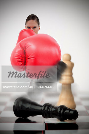 Woman in boxing gloves knocking over chess pieces on chess board