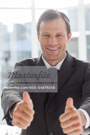 Smiling confident businessman giving thumbs up in his office