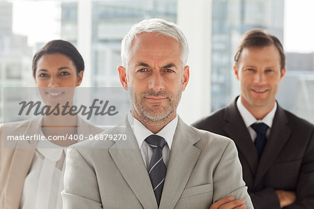 Businessman standing with colleagues behind with arms crossed