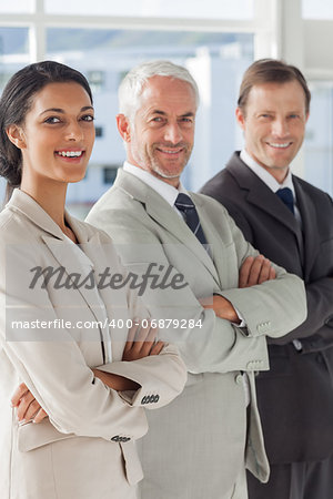 Three smiling business people standing together with their arms folded