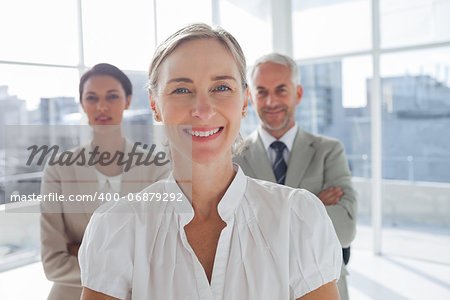 Smiling businesswoman standing in front of colleagues with arms crossed