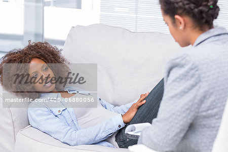 Woman lying on sofa and speaking to her therapist who takes notes