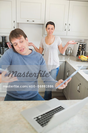 Man busy with technology while his wife wondering why in kitchen