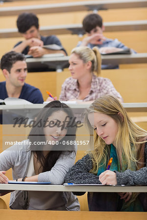 Students sitting in a lecture hall while studying while using a tablet pc and talking