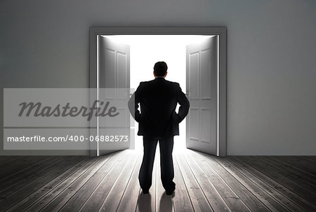 Businessman looking at door showing bright light in dull grey room