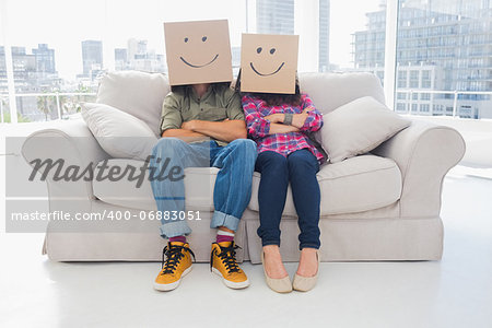 Silly employees with arms folded wearing boxes on their heads with smiley faces on a couch