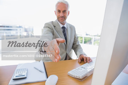 Happy businessman reaching arm out for handshake in his office