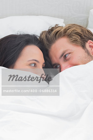 Couple under the quilt looking at each other in their bed