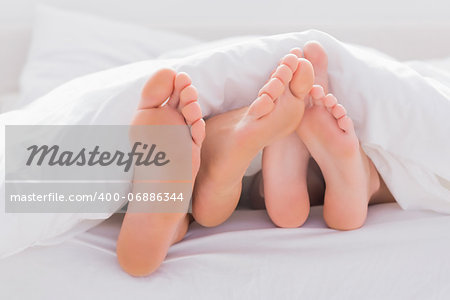 Couple rubbing their feet together under the duvet in bed