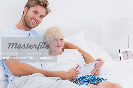 Father and his son using a tablet in bed