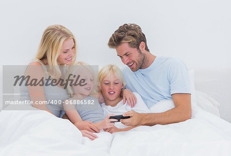 Beautiful family using a smartphone in bed