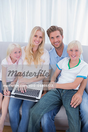 Smiling family using laptop in their living room and looking at camera