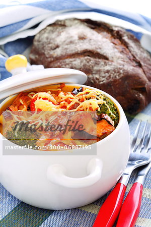 Pasta and vegetables baked with cheese in a white ceramic pot.