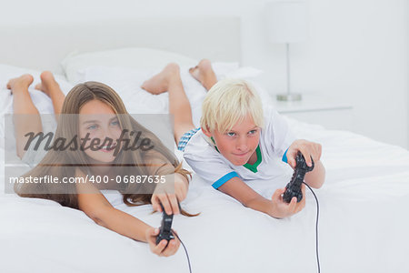 Siblings playing video games while they are lying on bed