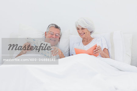 Mature man showing newspaper to his wife in bed