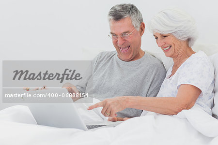 Mature man with wife pointing at a laptop in bed