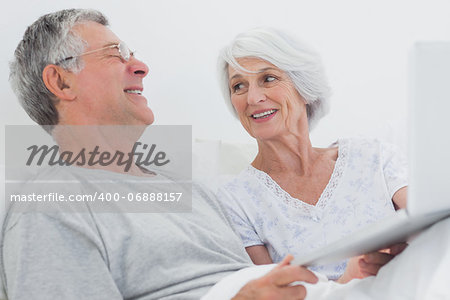 Cheerful mature couple using a laptop together in bed