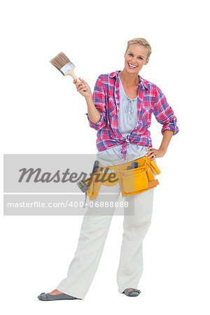 Happy woman holding paint brush wearing a tool belt on white background