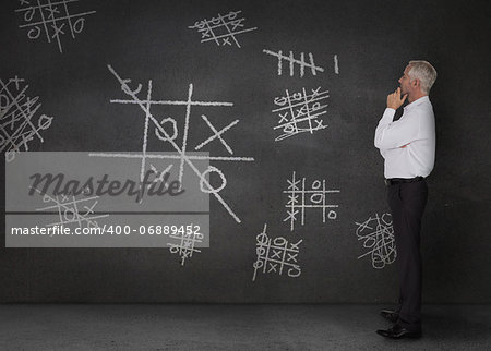 Doubtful businessman looking at tic-tac-toe drawn on the wall