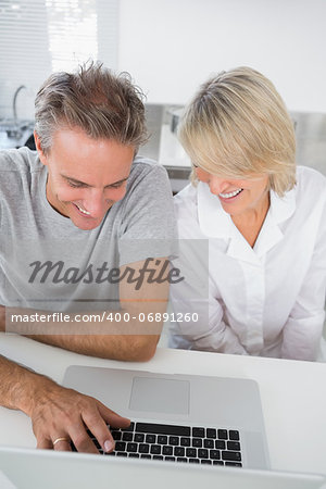 Happy couple using their laptop in the morning sitting at kitchen counter