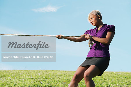 resolute business woman pulling rope against blue sky, symbol of power and determination. Copy space, side view