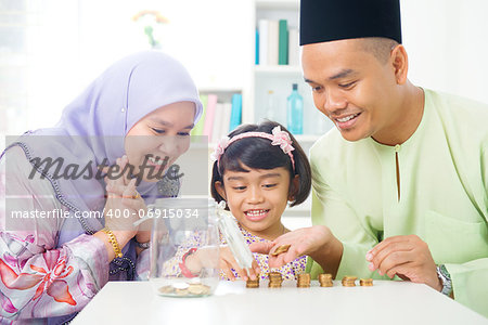 Islamic banking concept. Southeast Asian family counting money at home. Little Malay girl and parents saving money. Muslim father, mother and daughter living lifestyle.