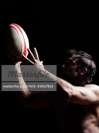 one caucasian sexy topless man portrait hugging a rugby ball on studio black background