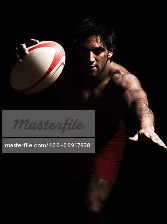 one caucasian sexy topless man scoring touchdown with  a rugby ball on studio black background