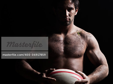 one caucasian sexy topless man portrait holding a rugby ball on studio black background