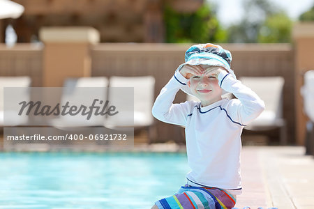 cute smiling caucasian boy sitting by the pool and enjoying summer vacation