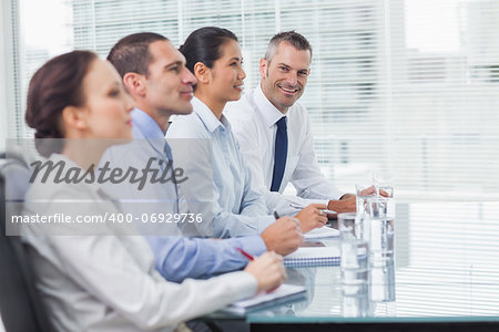 Businessman  in bright office smiling at camera while his colleagues listening