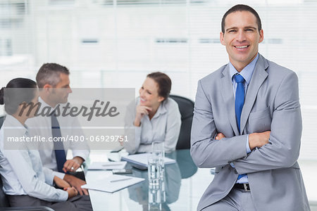 Smiling businessman in bright office posing while workmates talking together