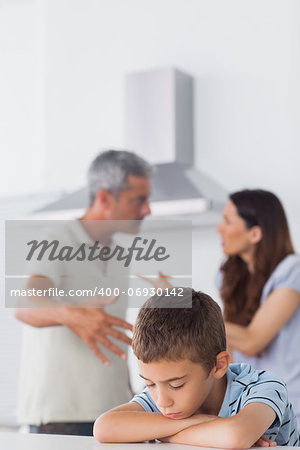 Couple having dispute in front of their sad son sitting in kitchen at home