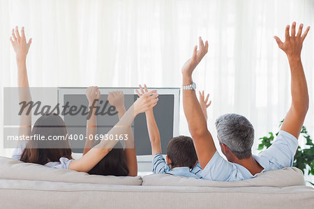 Family watching televison and rising theirs arms on sofa