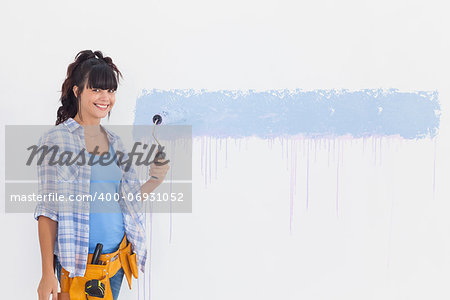 Woman painting wall blue and smiling at camera at home in empty room