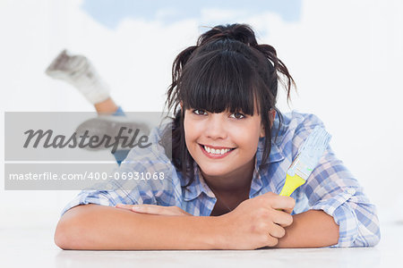 Happy woman lying on floor holding paint brush looking at camera