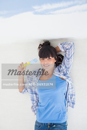 Attractive woman lying on floor holding paint brush smiling at camera overhead