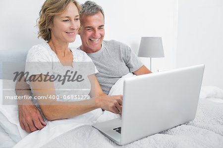 Smiling couple using their laptop together in bed at home in bedroom