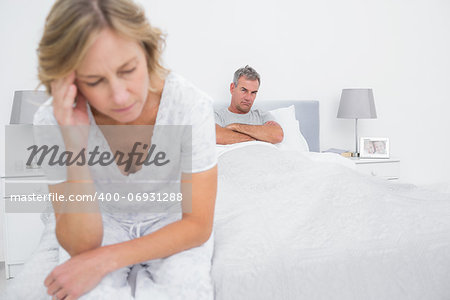 Unhappy couple sitting on opposite ends of bed after a fight in bedroom at home