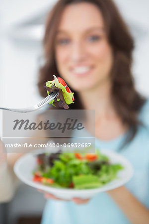 Healthy brunette in her kitchen offering salad to the camera