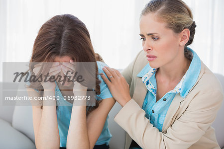 Crying woman with her concerned therapist sitting on the sofa