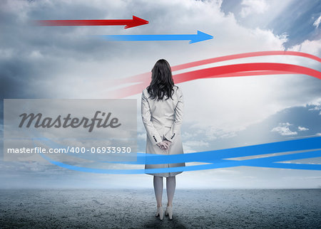 Businesswoman looking at red and blue arrows in cloudy desert landscape