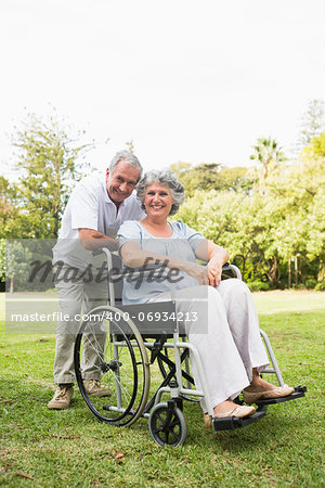 Happy mature woman in wheelchair with partner looking at camera in the park